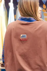 Remera tipo polo de manga larga con diseño de mangas raglán a rayas horizontales azules y blancas. El cuerpo de la prenda es blanco, con cuello polo y una pequeña estampa en el pecho. Confeccionada en tejido de algodón con spandex.