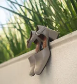 Zapato de cuero vacuno color gris topo, con talón descubierto y pulsera con hebilla. Tiene taco de madera forrado en cuero y suela de goma. La horma es de punta cuadrada, ancha y cómoda.
