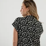 Blusa de mangas cortas con estampado de hojas en blanco y negro, cuello en V y cierre con botones.