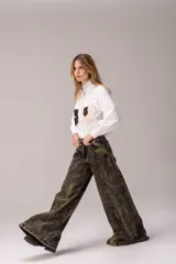 Camisa blanca de manga larga con cuello alto gorguera con volados y detalles de alforzas verticales en el frente. Cuenta con dos bolsillos en el pecho de pelo con estampado de vaca en tonos marrones y blancos.