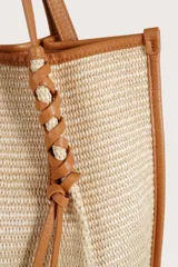 Bolsa tipo tote de textura tejida en color natural, con detalles de ribetes, asas y cordones decorativos en cuero sintético color suela.