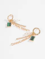 Aros colgantes dorados con diseño de argolla superior y múltiples dijes colgantes: una cadena de eslabones, una tira de strass, una perla pequeña y un dije rectangular de piedra verde.