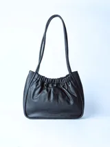 Bolso tipo tote bag de cuero negro, con diseño fruncido en la parte superior y dos asas delgadas de hombro. Presenta un acabado de cuero suave y arrugado.