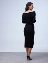Vestido midi de punto rib, color negro, con escote bote y cuello volcado. Presenta mangas largas y un diseño ajustado al cuerpo con tajo lateral en el ruedo.