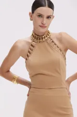 Top cropped color beige confeccionado en punto crepé, con cuello halter adornado con apliques dorados y aberturas caladas en los hombros.