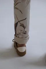 Pantalón de corte recto y ajuste holgado, confeccionado en tela beige con estampado floral en tonos marrones. Presenta cintura elástica con cordón ajustable y ruedos doblados.
