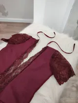 Body de lycra color bordó con mangas cortas de encaje y detalle de encaje vertical en el frente. Presenta un diseño con espalda descubierta y tiras finas para atar en el cuello.
