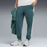 Pantalón de jogging Puma color verde esmeralda, con franjas laterales blancas y logo de la marca bordado en la pierna. Presenta puños elásticos en los tobillos y bolsillos laterales.