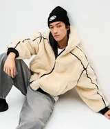 Campera de fleece color beige con diseño de paneles, costuras expuestas en color negro y cierre frontal. Posee cuello alto, mangas largas con puños elásticos y forro interior.