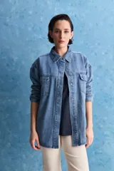 Sobrecamisa de denim de calce amplio y color azul, con cuello clásico, cierre frontal con broches metálicos y bolsillos delanteros con solapa.