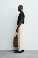 Pantalón de algodón color beige claro, de corte recto (regular fit), con pespuntes en hilo contrastante oscuro. Presenta bolsillos delanteros y bolsillos traseros de parche.