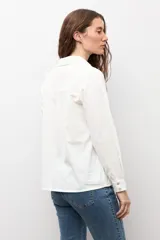 Camisa blanca de manga larga con frente de tela broderie con diseño de rombos calados y espalda lisa. Presenta cuello clásico y cierre frontal con botones.