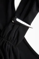 Top negro de punto suave, con escote asimétrico estilo halter y una tira ancha tipo fular sujeta con un detalle metálico decorativo. Presenta frunces laterales que generan un efecto drapeado sutil.