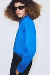 Jersey de punto con cuello tipo polo, manga larga con puños y cierre frontal con botones. Presenta un bolsillo de plastrón en el pecho y diseño de corte holgado.