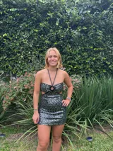 Vestido corto de satén color verde azulado (teal) con escote strapless y detalle de frunce central con argolla. Presenta tirantes finos que se atan al cuello y aberturas laterales en la cintura.