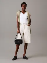 Cartera tipo cámara convertible Calvin Klein negra, con textura monograma en el bolsillo frontal y logo metálico plateado. Incluye dos correas desmontables: una ancha ajustable para cruzar y una fina para llevar al hombro.