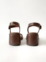 Sandalias de cuero color chocolate, con taco cuadrado de 6 cm, tira ancha en la parte delantera y tira en el tobillo con hebilla metálica ajustable.