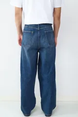 Jean de corte baggy y silueta holgada, confeccionado en denim de algodón color azul oscuro con efecto lavado. Presenta diseño clásico de cinco bolsillos, cintura con trabillas y cierre frontal con botón y cremallera.