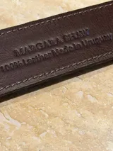 Cinto de cuero negro con hebilla ovalada metálica dorada grabada con detalles florales.