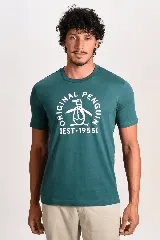 Remera verde oscuro con cuello redondo y mangas cortas, con estampa frontal circular en color blanco del logo y la marca Original Penguin junto al año 1955.