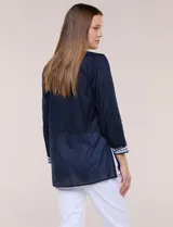 Blusa de corte holgado de inspiración étnica con bordados ornamentales blancos a contraste. Presenta escote en V pronunciado con pechera bordada con motivos arabescos y florales, mangas largas y aberturas laterales en el ruedo.