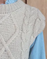 Chaleco de punto gris oscuro con diseño de trenzas y rombos en relieve, cuello redondo y terminaciones acanaladas.