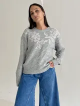 Sweater de punto color beige con cuello redondo, manga larga y detalle de bordado floral en la parte superior del pecho.