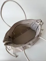 Bolso grande de cuero marrón con textura tipo cocodrilo, estructura rígida y asas para llevar al hombro. Tiene una tira con tachas y hebillas en cada extremo, también lleva lazos en los costados.