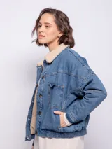 Campera de jean negra con cuello de corderito color crema, cierre frontal con botones metálicos, bolsillos frontales y laterales, y elástico en la cintura.