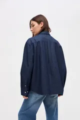 Camisa de algodón en color celeste claro, con cuello solapa, cierre frontal de botones y bordado pequeño en el pecho. Presenta un corte holgado y mangas largas.