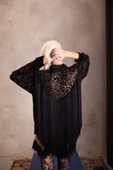 Camisa negra de corte recto con cuello clásico y botones frontales. Presenta mangas largas con puños abotonados y un acabado integral de flecos de seda que aportan movimiento y brillo a la prenda.