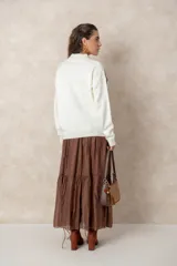 Buzo de tejido de punto color blanco, con cuello alto acanalado y mangas largas con puños ajustados. Presenta un diseño de flor grande en color chocolate aplicado en el frente.