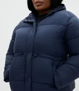 Campera puffer acolchada color azul marino, con capucha, cierre frontal con broches a presión, bolsillos laterales y cordón regulador en la cintura para ajuste entallado.