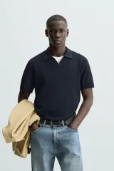 Jersey de punto color verde oliva, de calce relajado (relaxed fit), con cuello solapa y abertura frontal en forma de V. Es de manga corta y presenta acabados en rib en puños y ruedo.