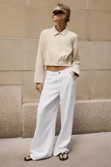Camisa crop de manga larga con cuello solapa y cierre frontal de botones, confeccionada en tejido sintético con efecto piel color beige.