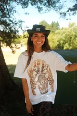 Remera oversize color marrón claro con estampado frontal de un paisaje desértico con palmeras y un camello.