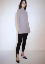 Jersey de punto acanalado color beige, con cuello alto y cierre frontal parcial. Presenta un diseño entallado de largo medio y mangas largas con terminación acampanada.
