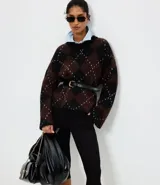 Suéter de punto pesado con diseño de cuadros argyle en tonos marrón y negro, con detalles de puntos claros. Presenta un corte oversize, cuello redondo acanalado y mangas largas.