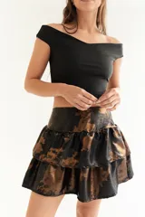 Pollera corta de tiro alto con diseño de volados escalonados que aportan volumen. Presenta un acabado satinado y tornasolado con un estampado abstracto en tonos oscuros y bronce.