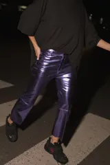 Pantalón de ecocuero color violeta metalizado, con corte capri semi oxford y tiro medio-alto. Presenta cierre frontal con botón metálico y bolsillos traseros.