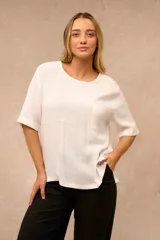 Blusa blanca de corte holgado con cuello redondo, mangas cortas con vuelta y un bolsillo aplicado en el pecho.