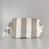 Neceser rectangular de tela a rayas verticales grises y blancas, con parche de cuero marrón con logo de la marca.