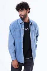Camisa de jean de manga larga en tono azul claro, con cuello clásico, cierre frontal con botones y dos bolsillos delanteros con solapa.