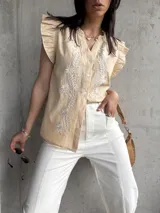 Blusa color beige con bordado floral blanco en el frente, cuello en V y mangas cortas con volados.