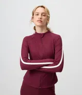 Campera deportiva Get Over en microfibra bordó, de ajuste próximo al cuerpo, con cuello alto, cierre frontal por cremallera y franja blanca contrastante desde los hombros hasta los puños.