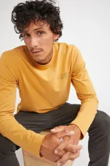 Remera de manga larga color mostaza, con cuello redondo y estampado frontal con las siglas MST en contorno verde.