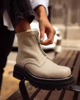 Botas de caña corta color beige, confeccionadas en cuero con textura granulada. Presentan cierre frontal central, suela track negra de goma con costuras blancas visibles y tirador en la parte trasera.