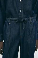 Pantalón de jean estilo wide leg en color azul oscuro, con cintura elástica y cordón ajustable. Presenta costuras verticales decorativas en el frente y bolsillos laterales.