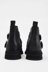 Botín de cuero vacuno color marrón, con punta fina y detalle de tachas metálicas en la parte superior. Presenta una suela de plataforma plana de color negro.