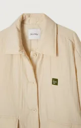 Chaqueta capitoneada color crema, de corte oversize, con cuello camisero, cierre frontal con botones a presión, bolsillos de parche y puños con abertura.